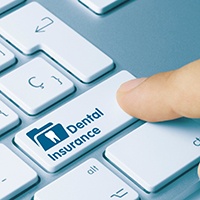 Finger pressing “dental insurance” button on computer keyboard
